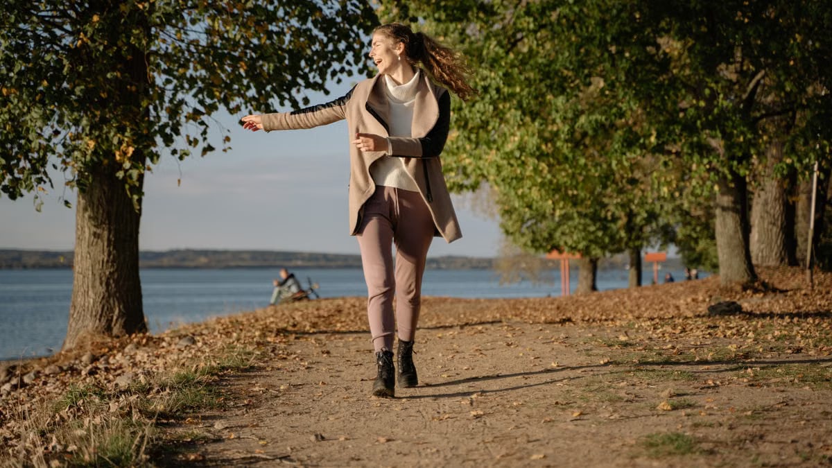 Woman enjoying a leisurely walk on a lakeside path in autumn with vibrant foliage.